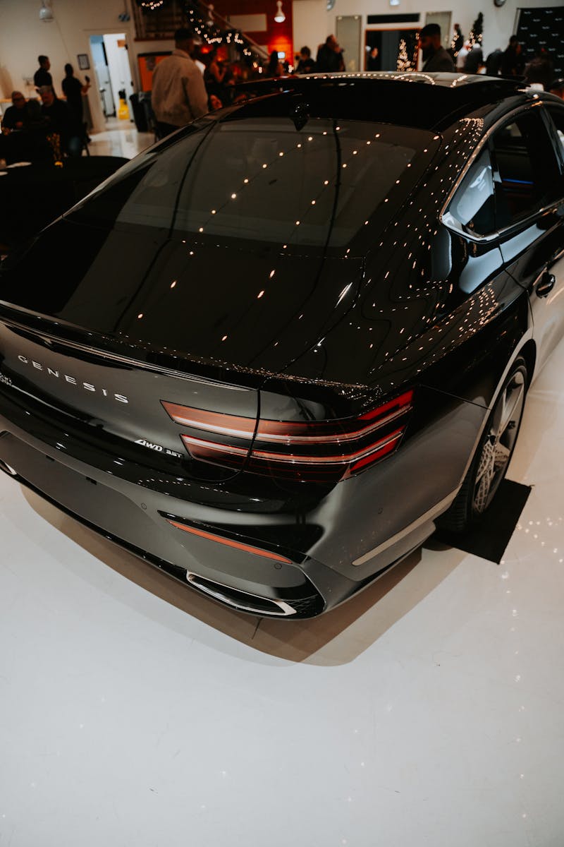 A stylish black Genesis G80 displayed in an indoor car showroom with reflective lighting.